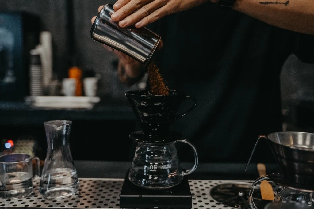 Manos sirviendo café molido en un dripper V60 negro sobre báscula, preparación pour-over